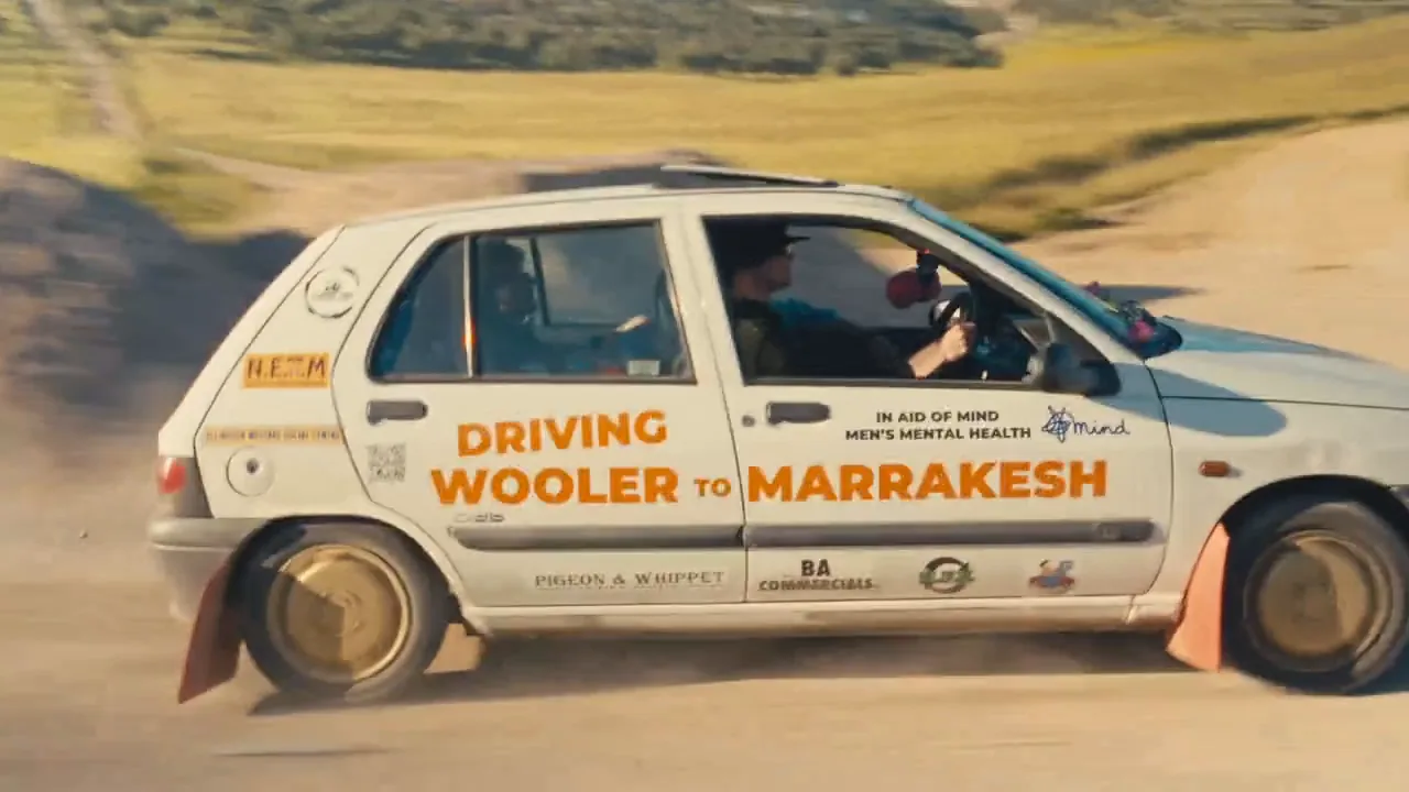 A white Renault Clio with Driving Wooler to Marrakesh on its doors, sliding on a dusty track.